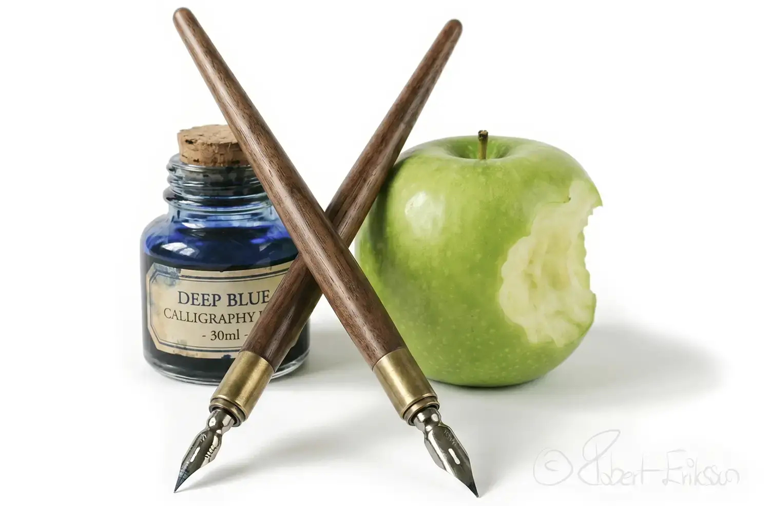 Kalligrafipennor som är korsade bläckbehållare och ett grönt äpple